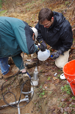 Zhenming Wang and Seth Carpenter of the KGS Geologic Hazards Section install one of the instruments at the new seismic station in a PVC-lined hole drilled behind the Perry County Public Library for the station.