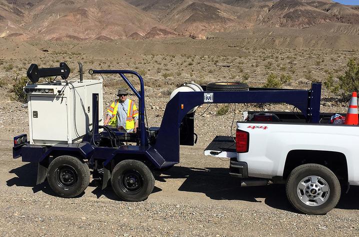 A photo of Ed Woolery in a desert landscape behind a large white piece of equipment. 